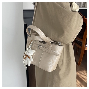 Detail of cream glossy bucket bag featuring a plush bear charm and leather strap