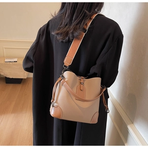 Close-up of khaki pebbled leather bucket bag featuring a wide contrast woven strap and drawstring