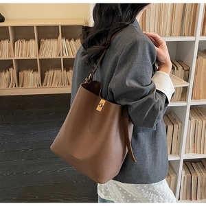 Brown lychee leather bucket bag with gold clasp shown on model in a library setting