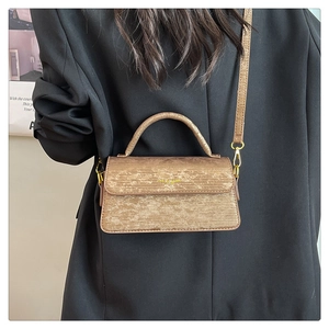 Detail of a bronze brown textured crossbody bag with metallic finish and top handle on model