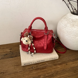 Detail of red metallic Boston bag with cute plush bear charm on an old vintage book