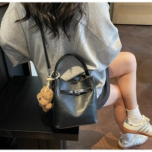 Detail of a black leather bucket bag with silver metal buckle and brown bear charm on model