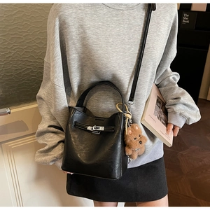 Detail of black bucket bag with lychee texture, silver twist lock and puppy pendant