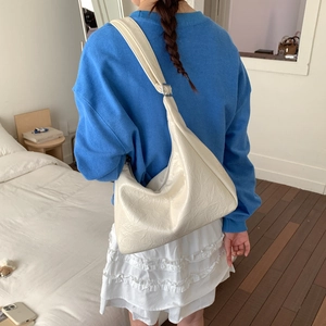 Sac hobo plissé en cuir crème porté par un mannequin dans une chambre lumineuse