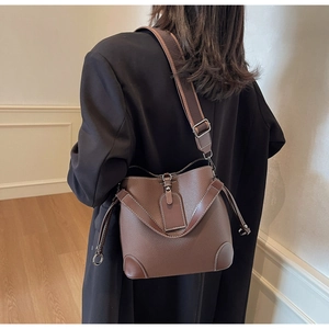 Detail of a brown lychee pattern bucket bag with a wide fabric strap on a female model