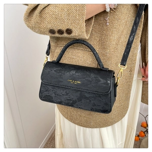 Detail of black crossbody bag featuring gold hardware and elegant textured surface