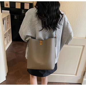 Chic taupe leather bucket bag shown on shoulder in a modern indoor lifestyle setting