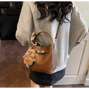 Detail of a brown bucket bag with a plush bear charm worn by a model in a modern room