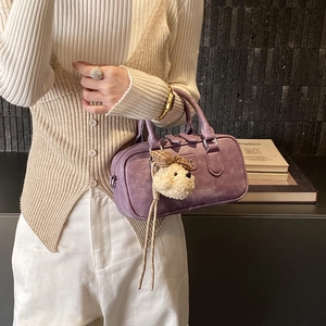 Close-up of purple faux suede Boston bag with silver buckles and plush dog charm