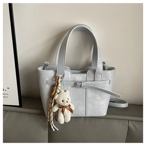 Detail of light blue faux leather bucket bag with braided strap and plush bear charm