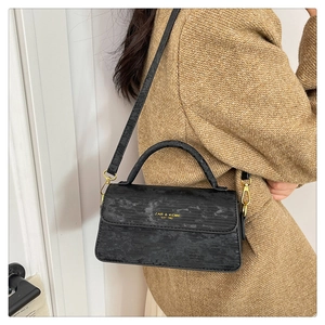Detail of black textured leather bag with gold logo and elegant crossbody strap