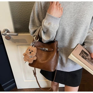 Detail of a brown retro bucket bag with silver twist lock and cute plush bear charm