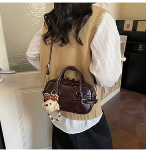Détail du sac Boston en cuir verni marron foncé avec breloque ours dans un décor chic