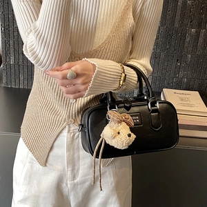 Detail of black Boston bag with fluffy dog charm shown on model in modern setting