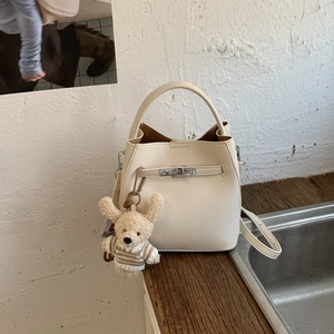 Detail of off-white lychee grain bucket bag with metal turn-lock and cute bear charm