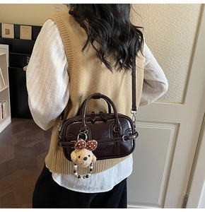 Détail du sac Boston marron brillant avec texture cuir lisse et breloque ours en peluche