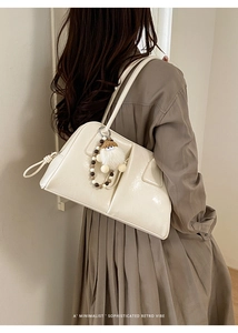 Cream white shoulder bag with smooth leather and a plush doll charm on a brown dress