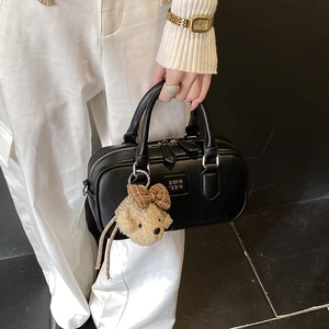 Detail of black leather Boston bag with plush bear charm and metallic brand embossing