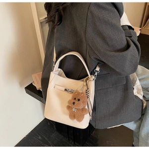Detail of cream leather bucket bag with silver turn-lock and brown teddy bear charm