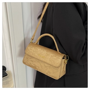 Detail of light beige textured crossbody bag with golden hardware and branded gold logo