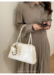 Close-up of a white leather tote bag featuring sleek vertical seams and a plush charm