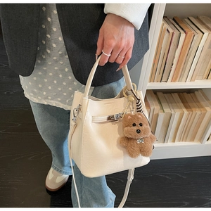 Detail of off-white lychee leather bucket bag with silver buckle and plush dog charm