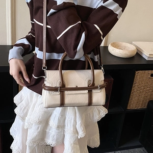 Detail of a beige leather crossbody bag with brown top handles worn by a fashion model