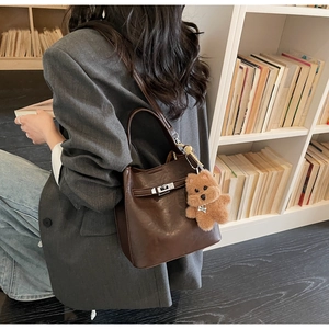 Detail of retro dark brown leather bucket bag with metal buckle and teddy bear charm