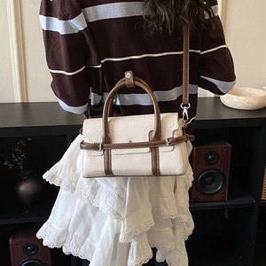 Detail view of a vintage beige and brown leather handbag worn by a model in casual attire