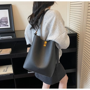 Detail view of black lychee grain leather bucket bag with a gold twist-lock on a shoulder