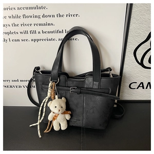Detail view of black faux leather bucket bag with cute bear charm and woven cord