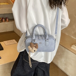 Detail of light blue crossbody bag with bear charm and tassel zipper on model