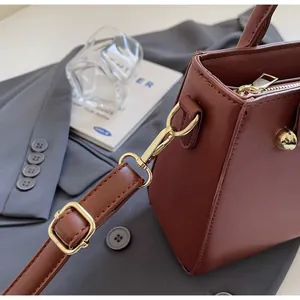Detail of burgundy leather crossbody bag with golden metal hooks and adjustable strap buckle