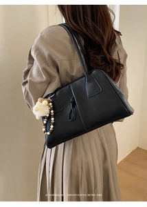 Detail of minimalist black faux leather shoulder bag with a beaded white fur ball charm
