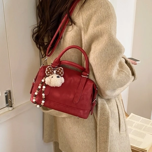 Detail view of red vintage tote bag with plush puppy charm on a camel wool coat