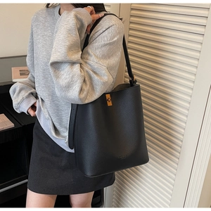 Detail of black pebbled leather bucket bag with gold lock worn by a model in casual setting