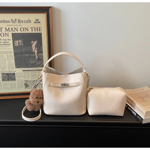 Detail of creamy white bucket bag with silver lock, mini pouch and plush bear charm