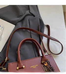Close-up of brown handbag with gold Lairuika logo, abacus pendant and tassel detail