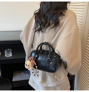Détail d'un sac Boston noir vintage avec bijou d'ours et boucle, porté par un mannequin