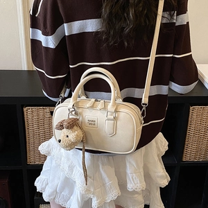 Chic cream white Boston bag with cute plush bear pendant shown on shoulder strap