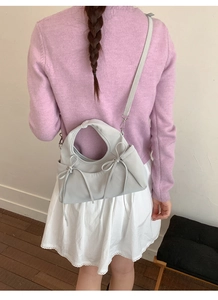 Dettaglio della borsa grigio chiaro con fiocco abbinata a cardigan viola e gonna a pieghe