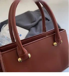Detailed close-up of golden spherical metal hardware on a reddish-brown leather handbag