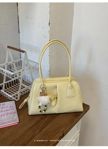 Close-up of a soft yellow underarm bag with a plush charm on a wooden table