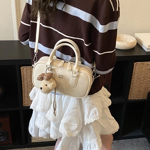 Detail of a beige Boston bag with dual handles and a cute plush charm accessory