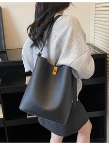 Minimalist black leather bucket shoulder bag with gold clasp shown on a model