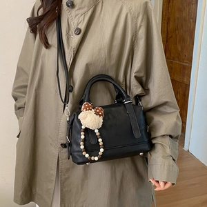 Detailed view of black leather tote bag with cute bear charm and adjustable shoulder strap