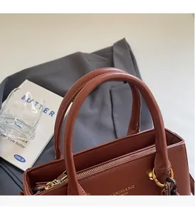 Detail of a brown leather handbag featuring gold logo and sturdy cylindrical dual handles