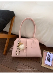 Detailed view of pink minimalist shoulder bag featuring a plush charm and wooden bead strap