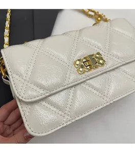Detail of white quilted crossbody bag with glossy texture and gold chain strap close-up