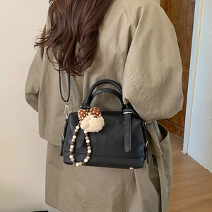 Detail of black matte leather tote bag with a cute plush puppy charm and shoulder strap